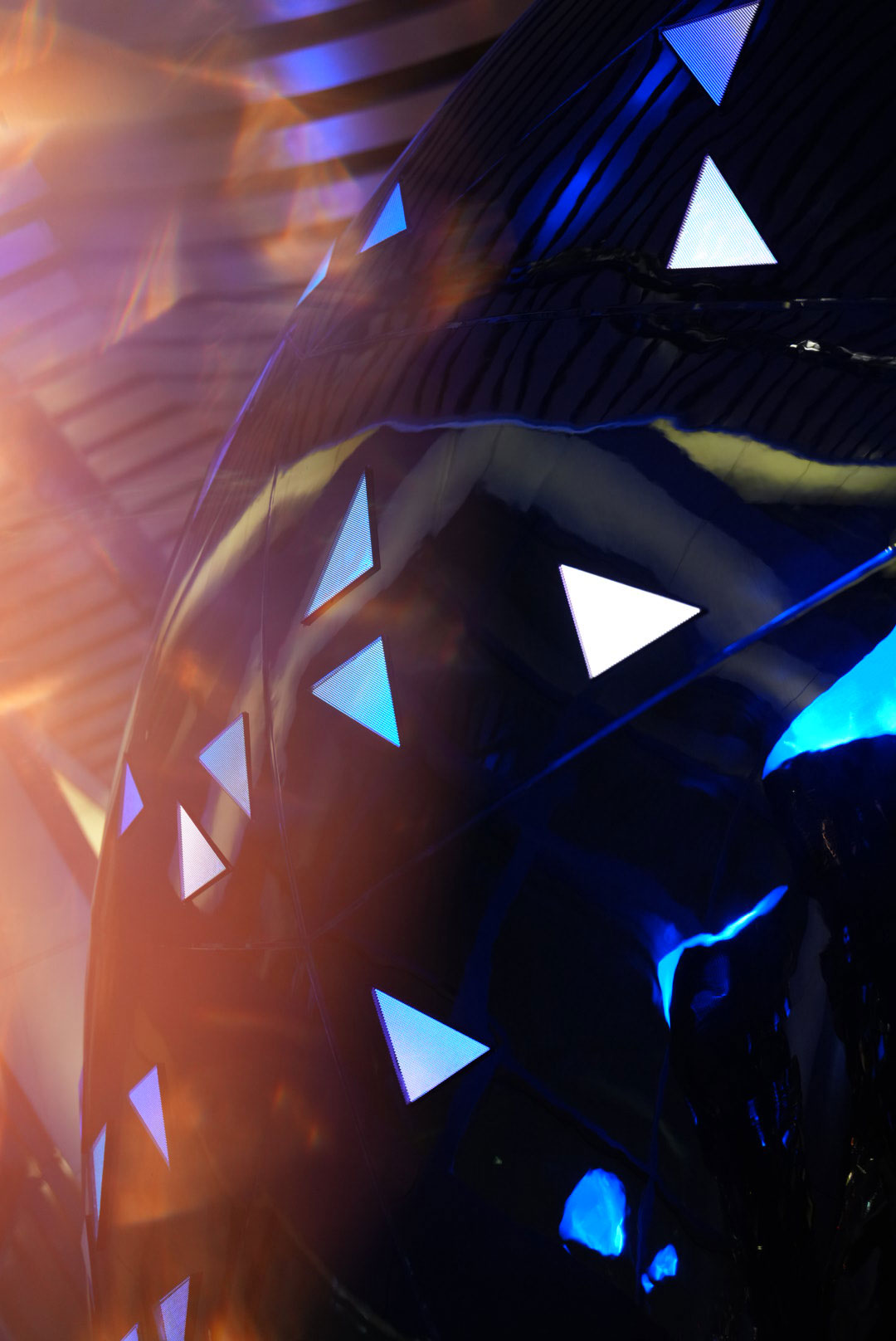 Close-up of Sphere’s sculptural exterior at One Za’abeel Dubai, showing glossy black reflective surfaces dotted with illuminated triangular light panels, with blue highlights and warm lens flares creating a futuristic, atmospheric glow.