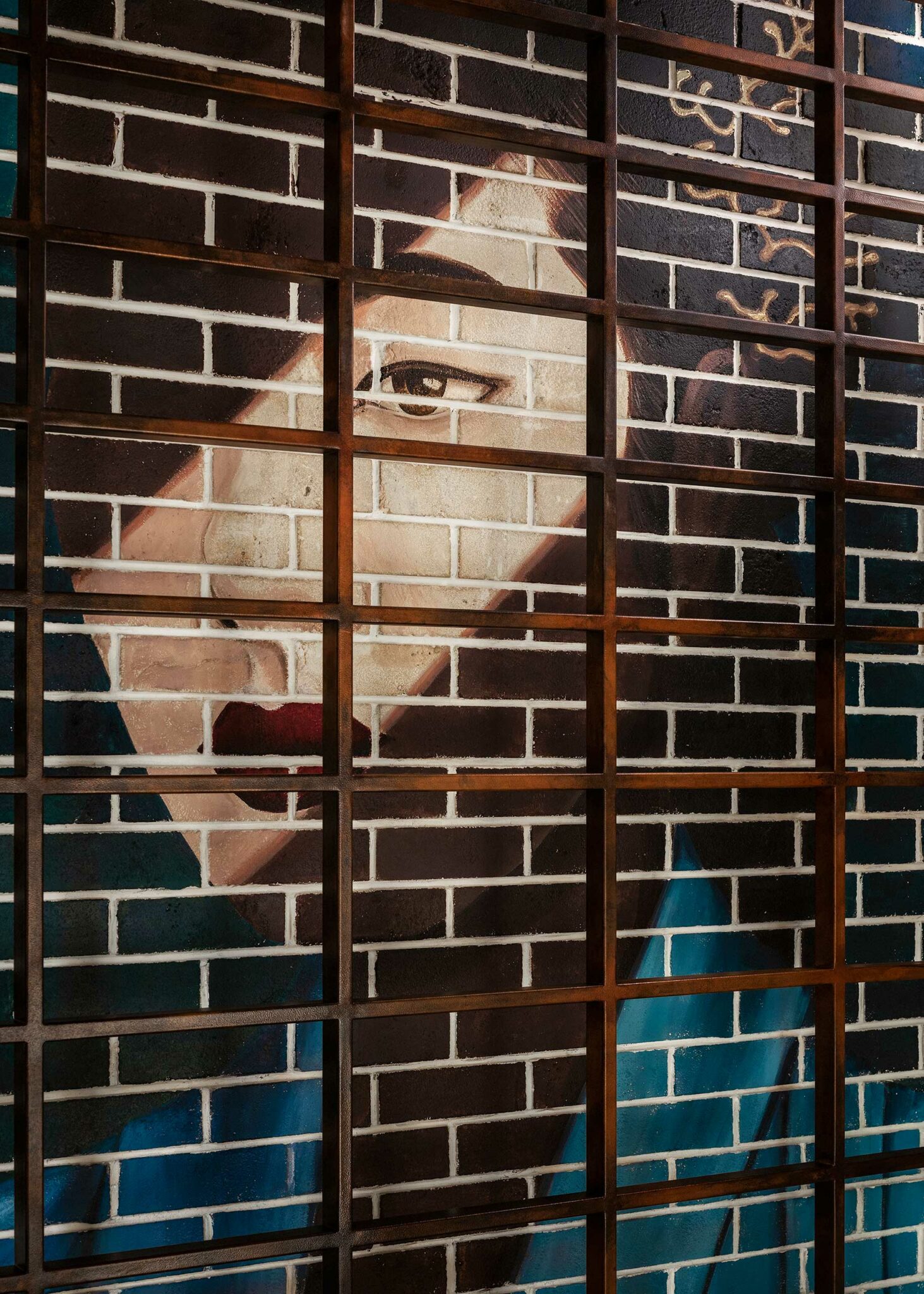 A close-up of the brick mural at Tapasake, One&Only Portonovi, depicting a stylised woman’s face framed by a geometric wooden grid—highlighting the venue’s art-led, contemporary approach to characterful hospitality storytelling.