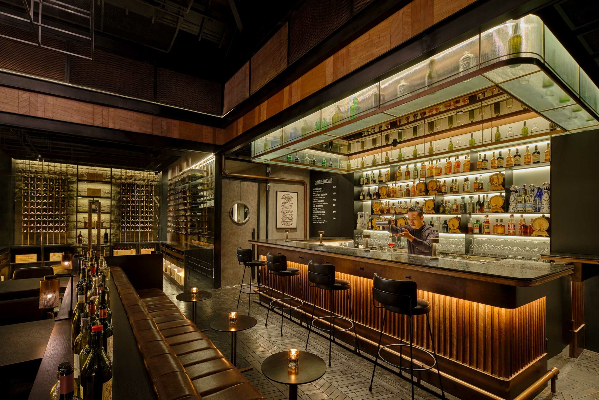 Moody, design-driven cocktail bar at Meatsmith Jakarta, with a floating bottle display, textured stone bar front, and intimate lighting that frames the mixologist’s workspace.