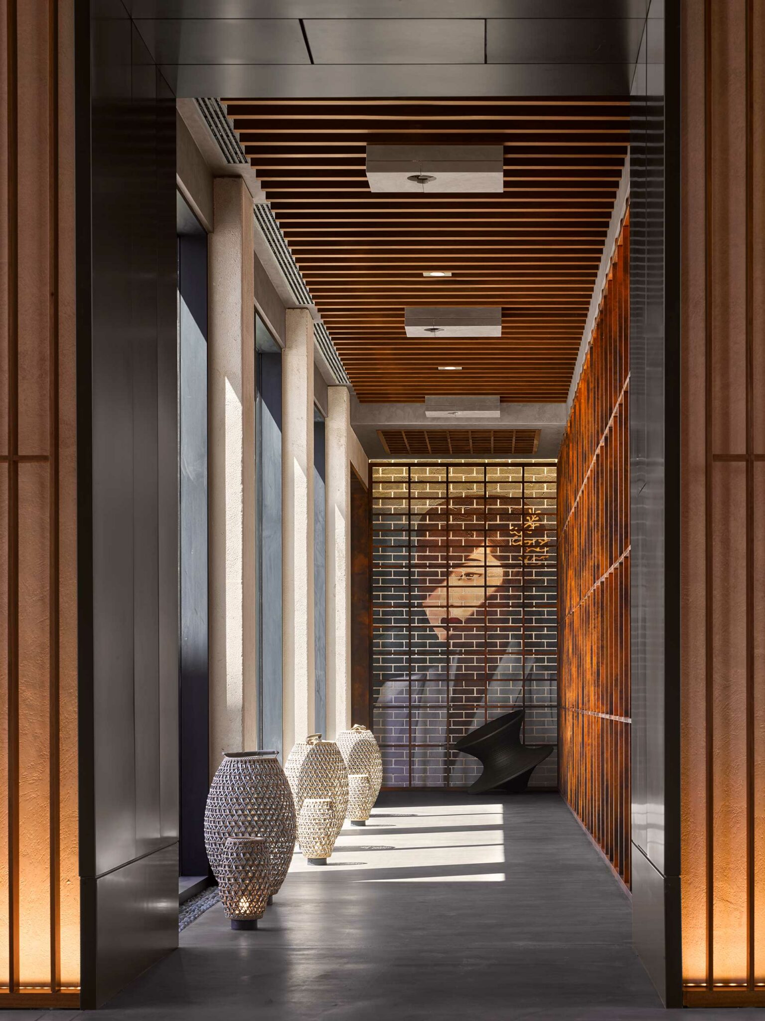 A sunlit corridor at Tapasake in One&Only Portonovi, featuring slatted wood ceilings, sculptural woven vases, and a brick mural of a woman