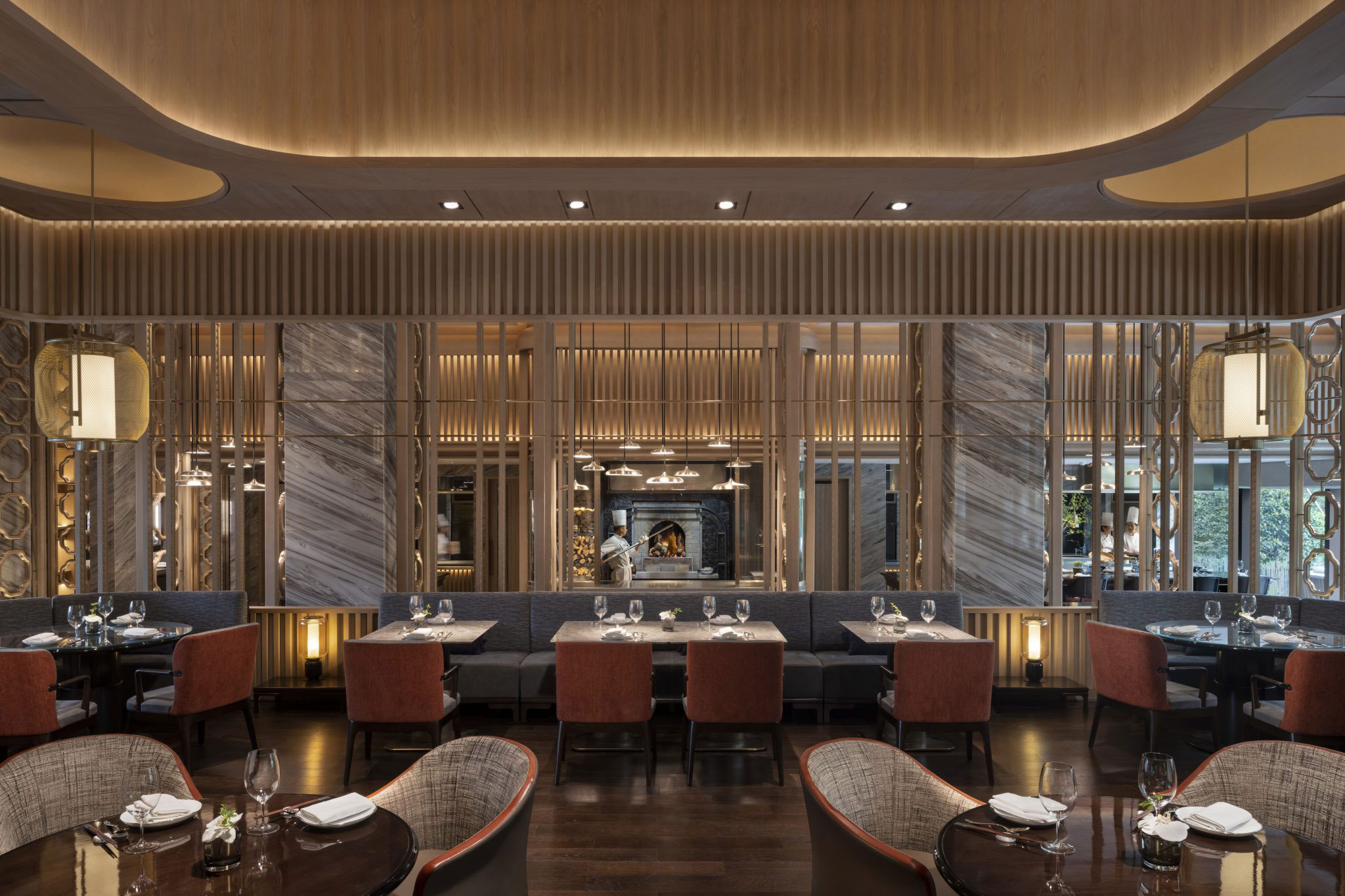 Elegant dining room at Xizhou Hall in Park Hyatt Suzhou featuring marble accents, warm wood panelling, modern lantern lighting, and neatly set tables overlooking the open kitchen on a platform inspired by the performance halls in China