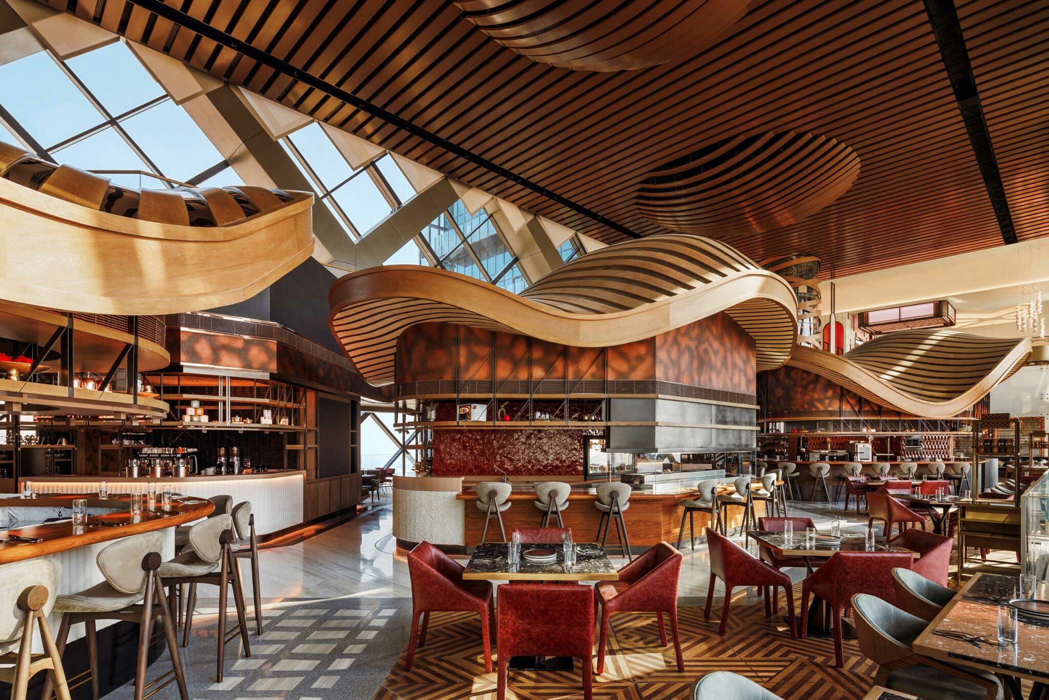 Luxury restaurant interior at Arrazuna in One Za’abeel Dubai, featuring sculptural wave-form wooden ceilings, contemporary open-kitchen stations, modern hospitality seating, and high-end restaurant design details.