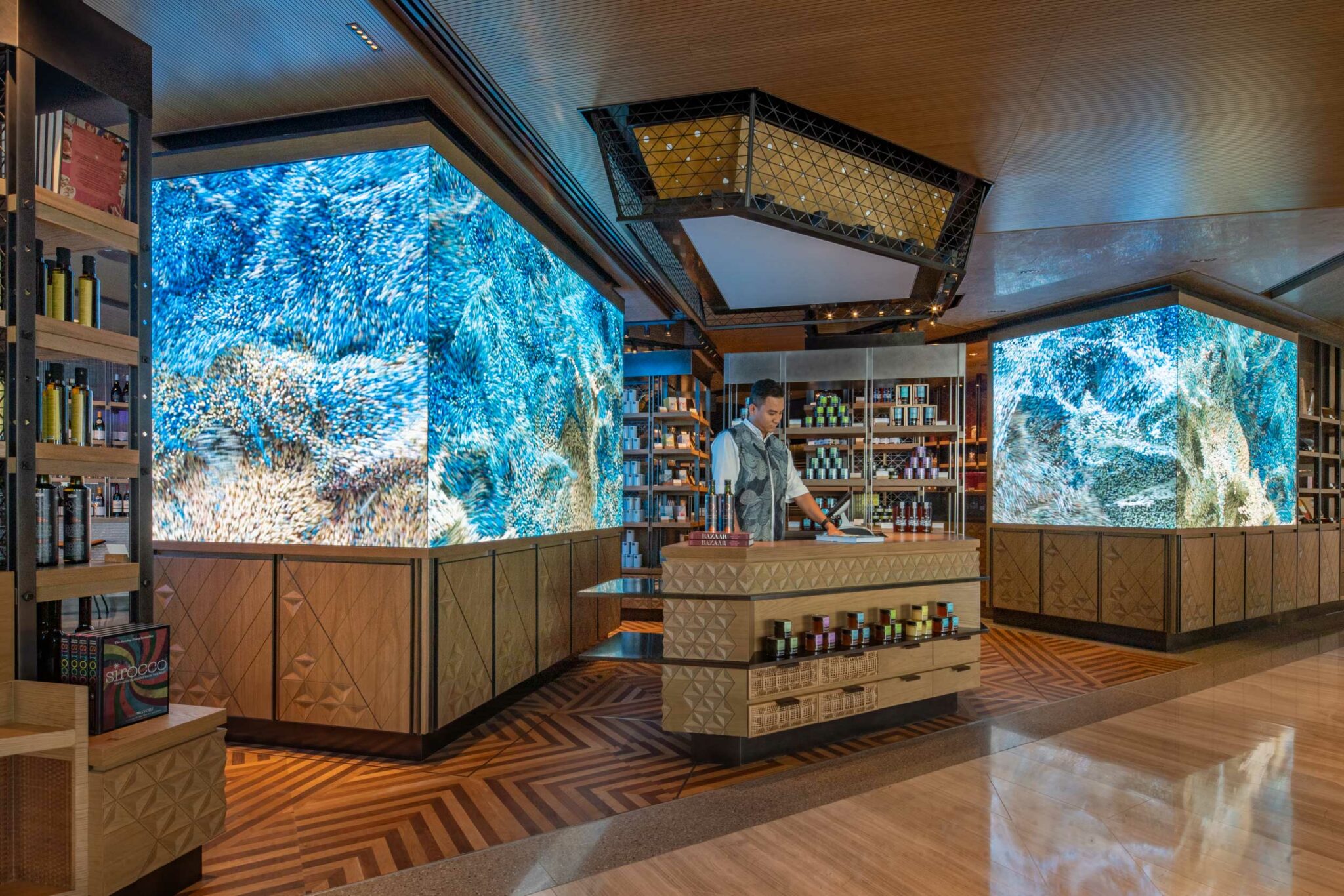 Arrazuna’s retail section featuring large immersive digital screens showing blue abstract visuals, geometric wood cabinetry, and a staff member working behind a counter stocked with premium products.