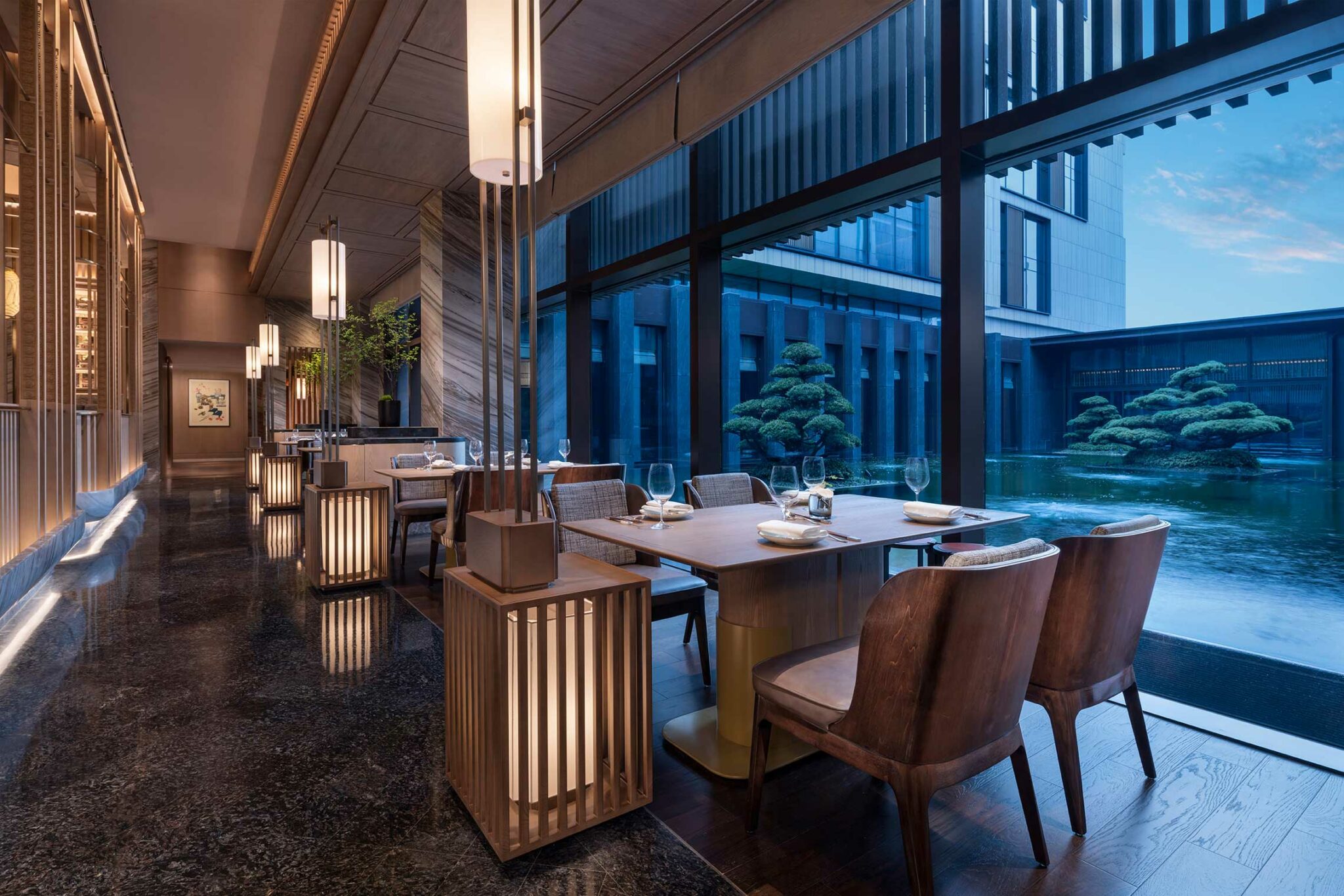Contemporary Chinese dining space at Park Hyatt Suzhou with lantern-style lighting, wooden tables, and serene views of the water garden and sculpted bonsai pines.