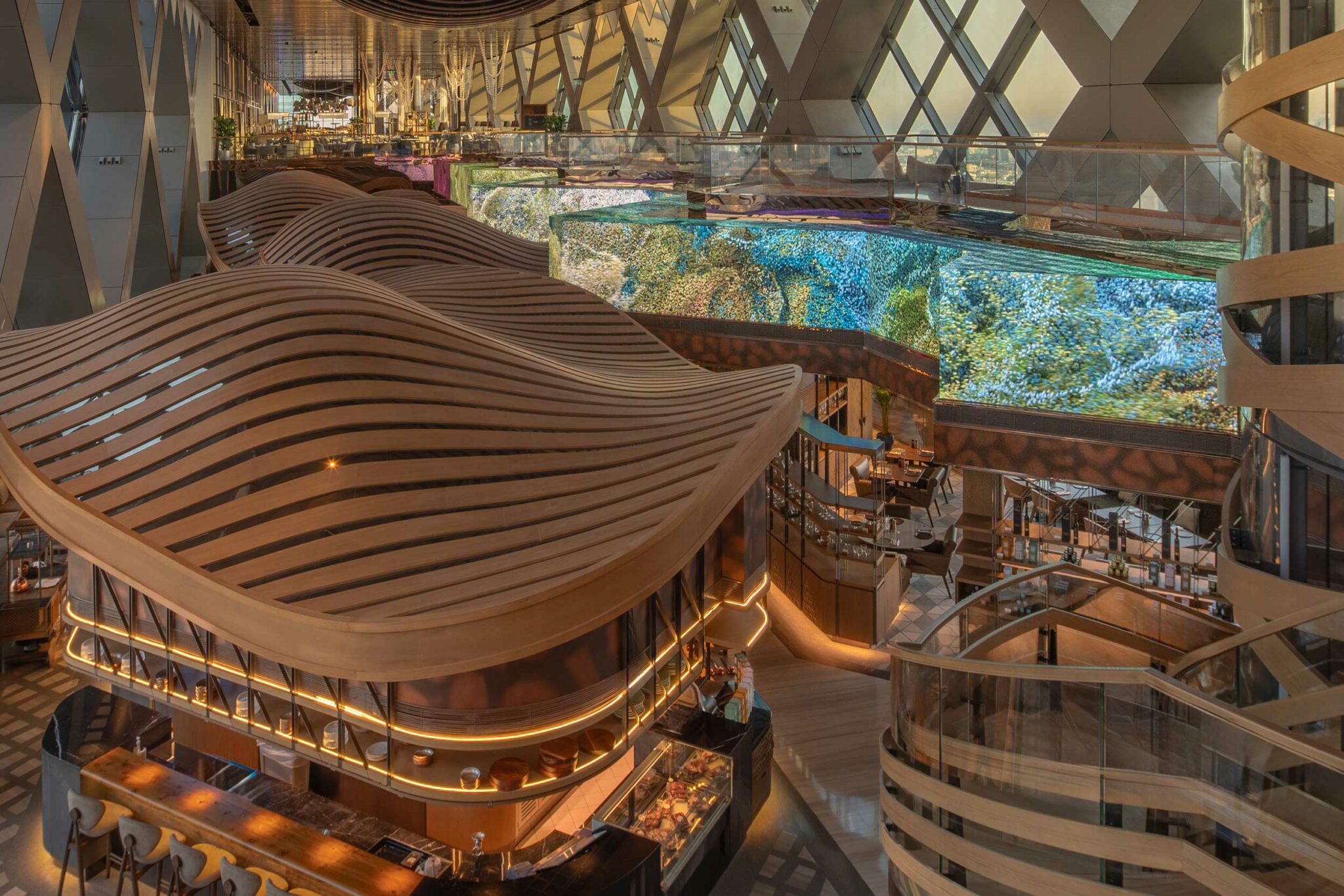 Luxurious, modern interior with wavy wooden textures and warm lighting. A large, vibrant digital art screen is mounted on the wall above seating areas. Bridge of Love