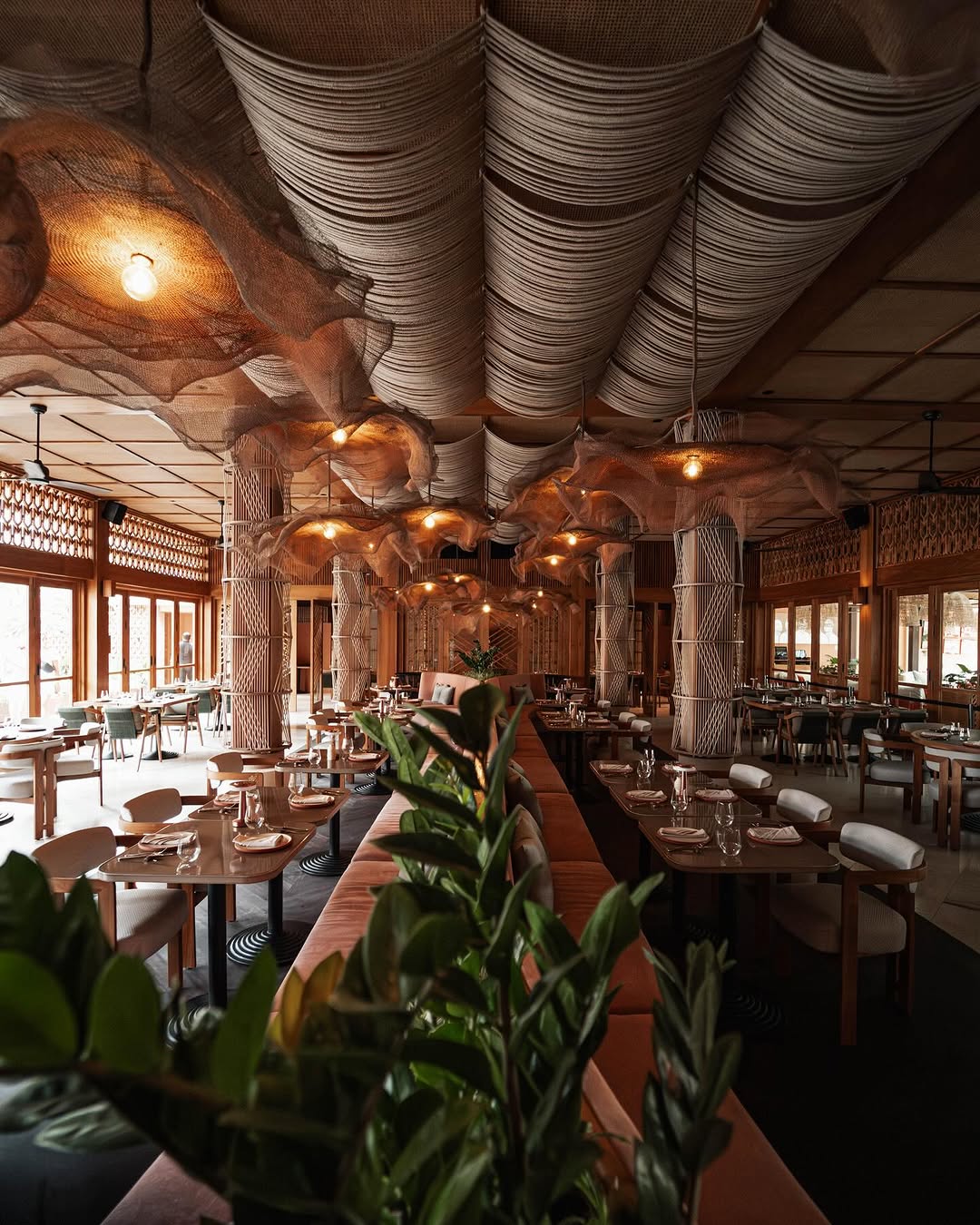 A warm, organic dining room featuring woven ceiling installations, sculptural columns wrapped in natural fibres, timber detailing, and soft seating—showcasing contemporary hospitality design rooted in craft, texture, and biophilic sensibilities. This is at desa kitsune in bali.