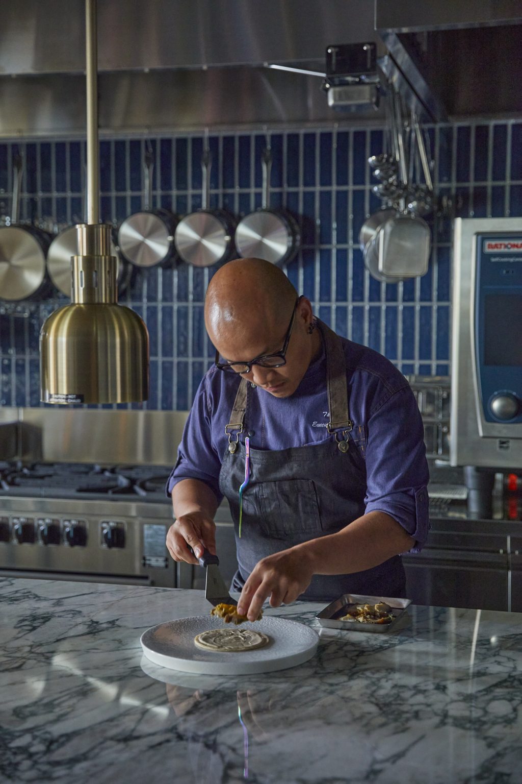 Chef plating a dish in the open kitchen at District, Kimpton Shinjuku Tokyo, reflecting the food-led identity and culinary direction shaped through market research and concept development.