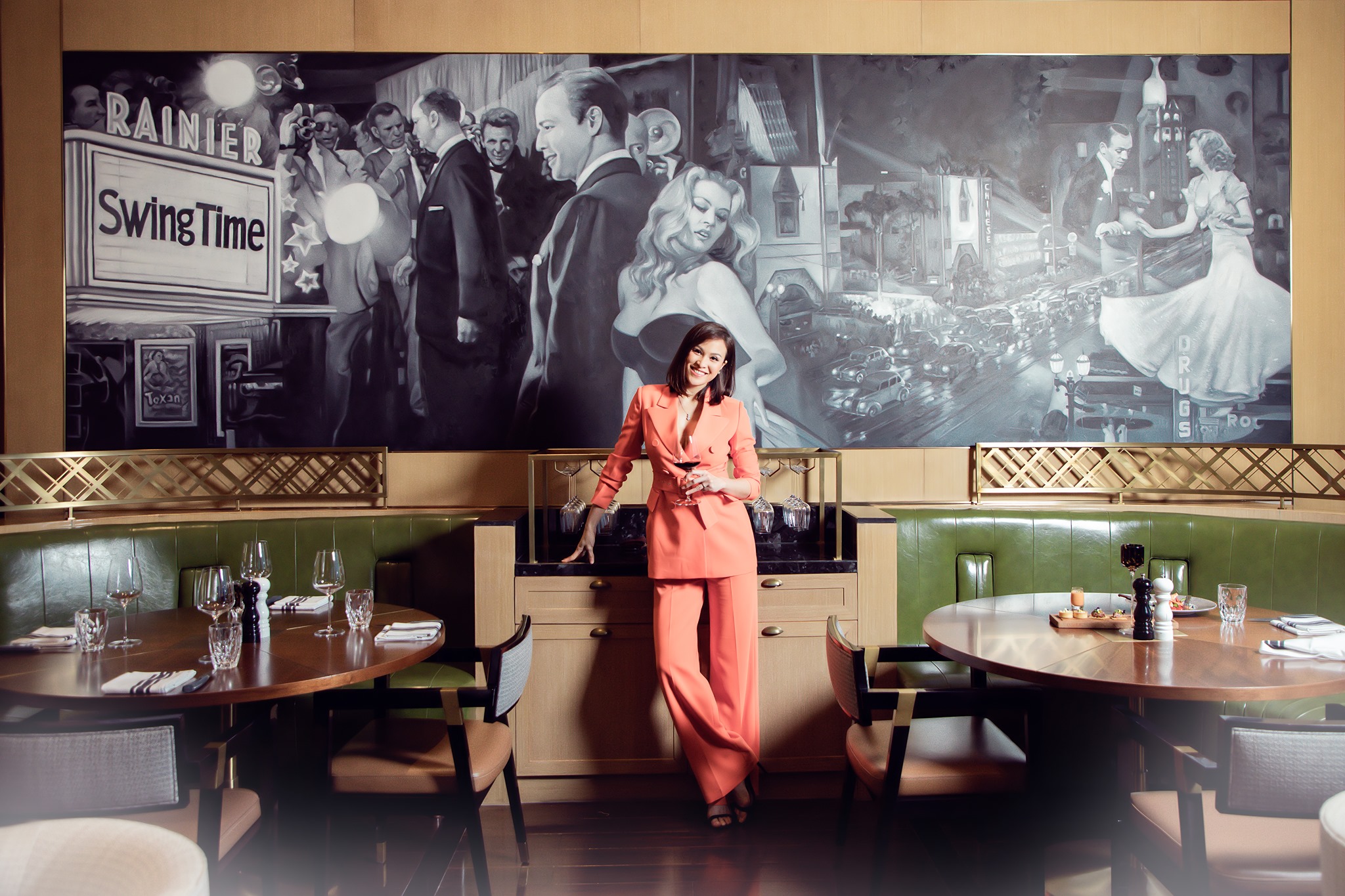 Dining area at Stellar Steakhouse featuring green leather banquette seating, timber tables, and a black-and-white mural backdrop framed by brass detailing.