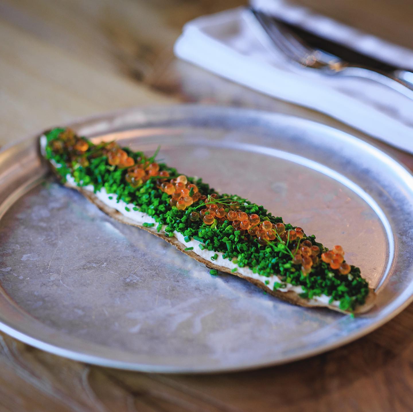 A plated dish at The Ledge by Dave Pynt featuring a crisp base topped with fresh herbs and roe, presented on minimalist tableware that reflects the restaurant’s refined, ingredient-driven dining experience.