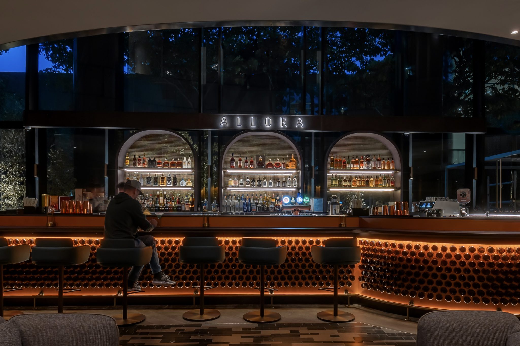 Allora Ristorante & Bar at Crowne Plaza Changi Airport, concept and branding consultancy by Social F+B, featuring a sculptural illuminated bar with arched back displays, warm bronze detailing, curated spirits, and an intimate, contemporary dining atmosphere designed for airport travellers.