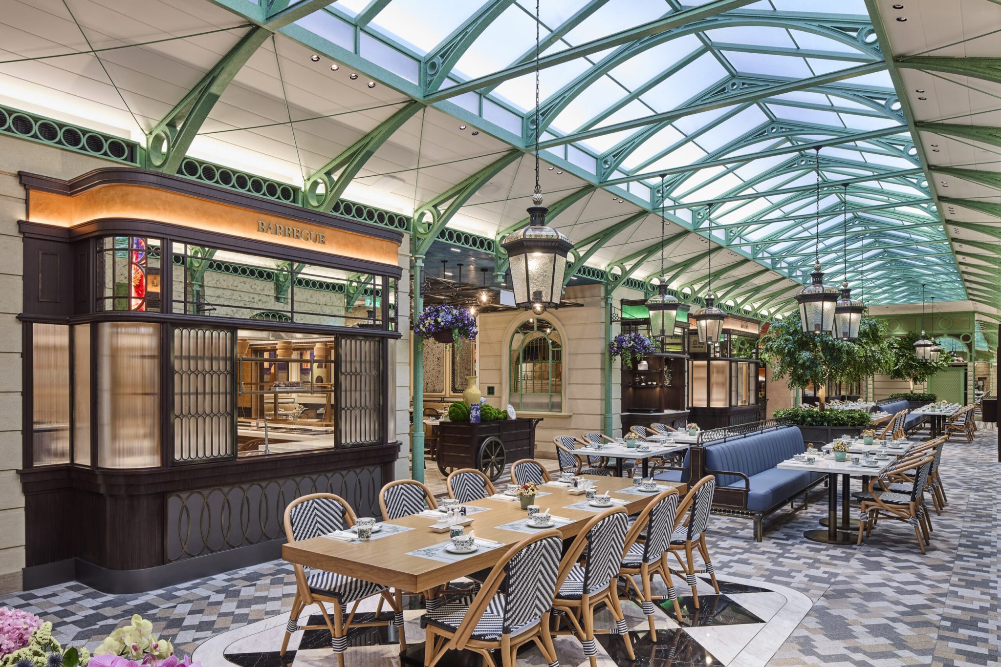 Main dining walkway at Chelsea Garden, Sands Resort Macao, designed by Social F+B as a destination food market inspired by Covent Garden, featuring live-show kitchen façades, patterned flooring, garden-style seating, hanging lanterns, and an open, market-like canopy that evokes a bustling London streetscape.