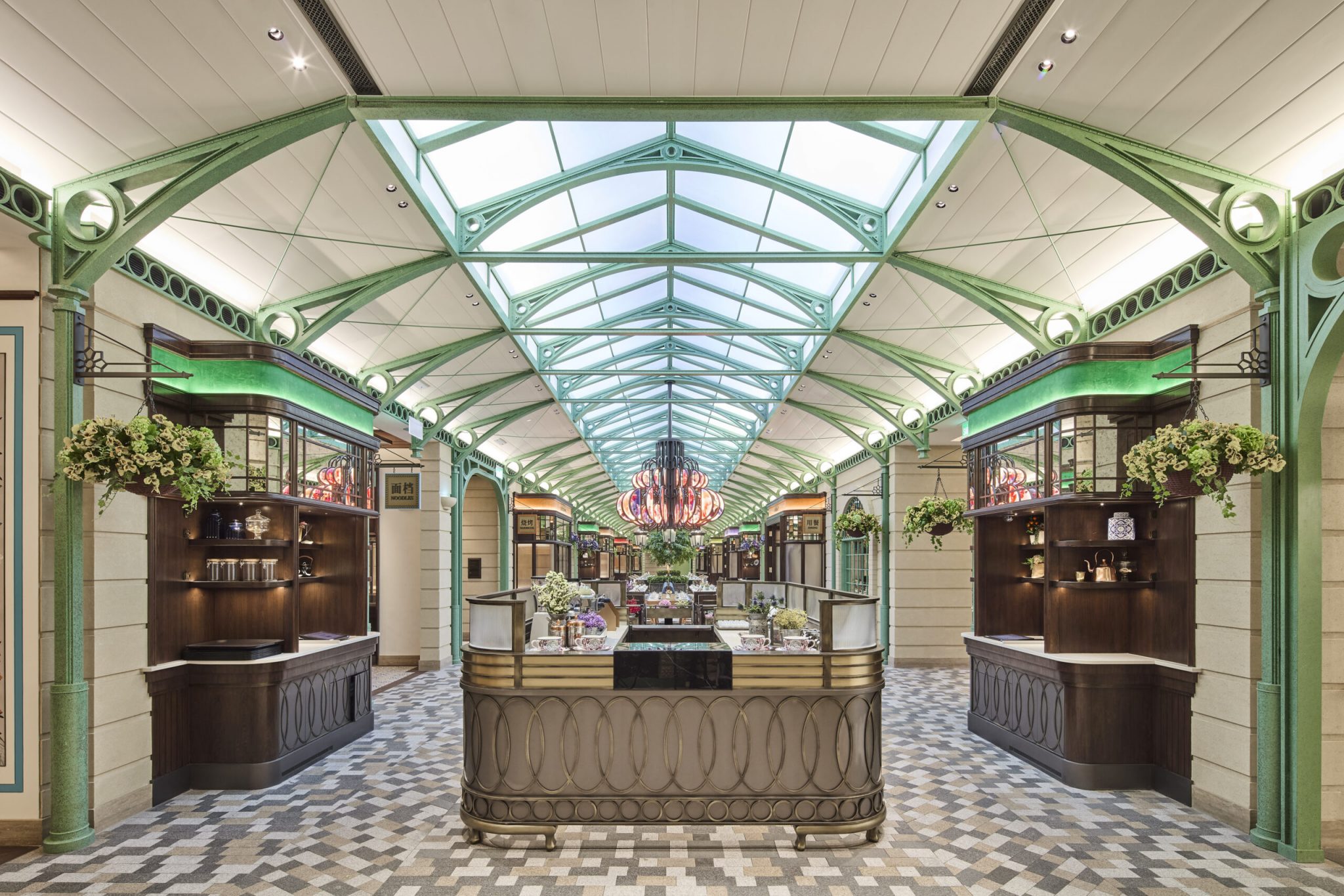 Symmetrical market hall at Chelsea Garden, Sands Resort Macao, designed by Social F+B to evoke London’s Covent Garden, featuring green steel trusses beneath a glass skylight, patterned stone flooring, flower carts, live-show kitchen stalls, and a central bespoke chandelier that anchors the destination food market experience.