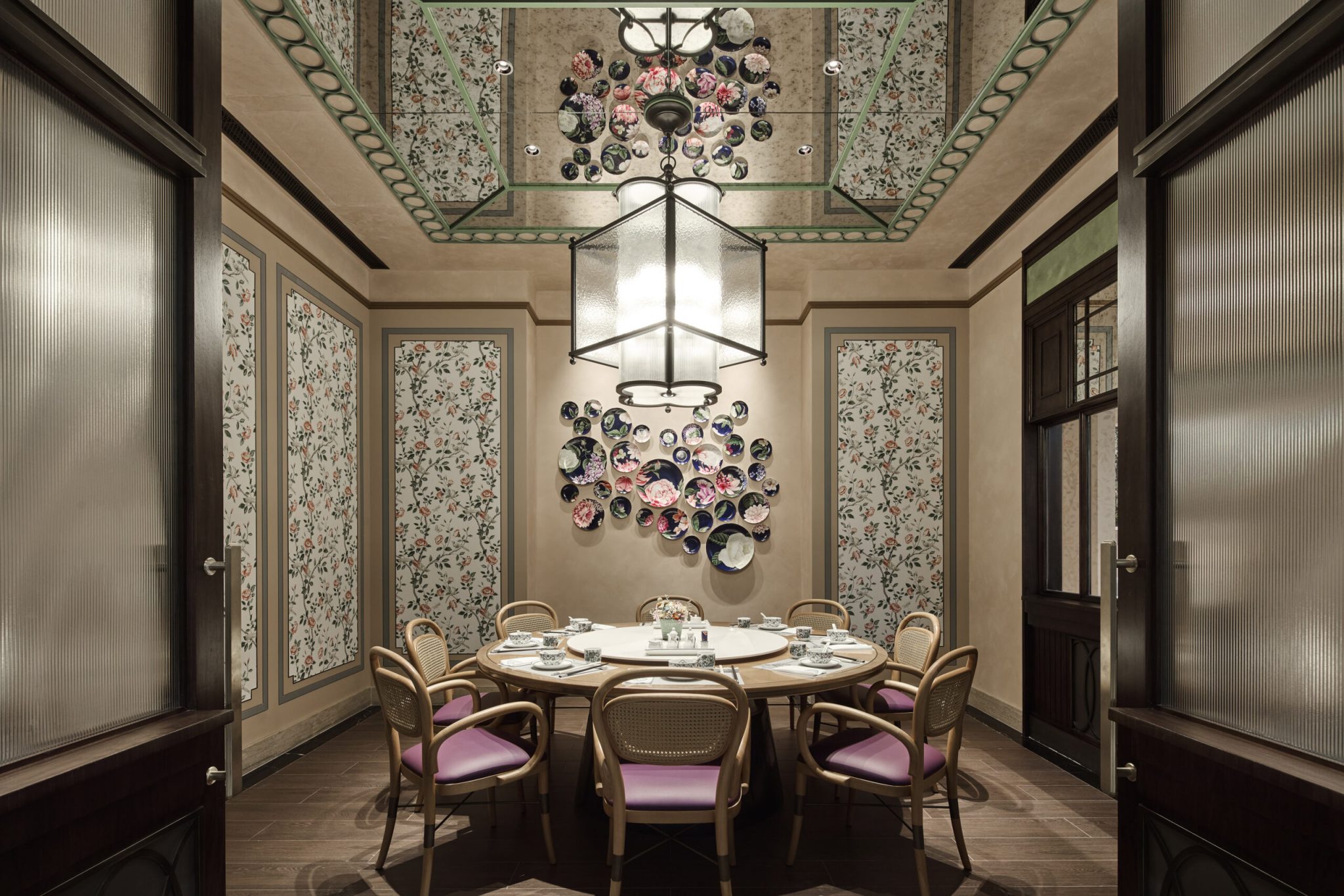 Private dining room at Chelsea Garden, Sands Resort Macao, designed by Social F+B, featuring a round communal table beneath a bespoke lantern chandelier, floral-patterned wall panels, curated ceramic plate art installation, and intimate seating that blends Covent Garden elegance with refined Hong Kong nostalgia.