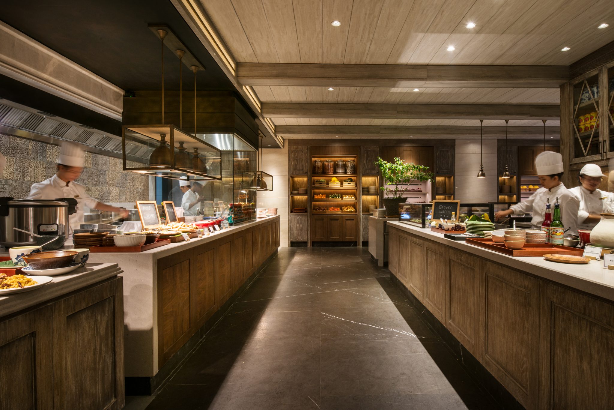 Open buffet kitchen at Grand Café, Grand Hyatt Jakarta, featuring timber-clad stations, live cooking counters, and a warm, market-style dining environment designed for all-day service.