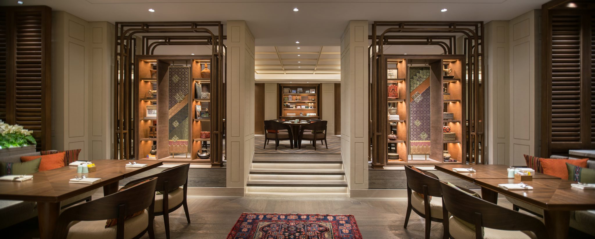 Dining area at Grand Café, Grand Hyatt Jakarta, featuring timber tables, layered seating zones, and display shelving with local textile accents within a refined all-day dining setting.