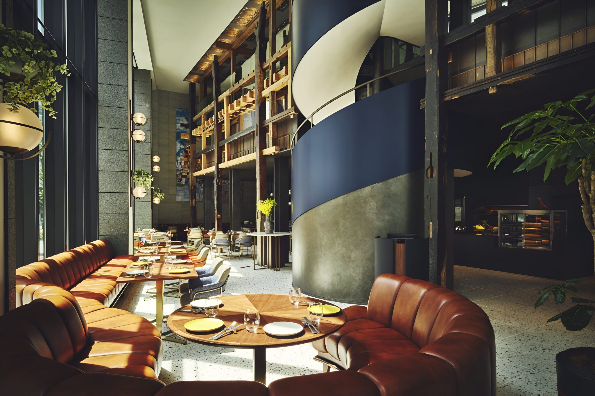 Double-height dining interior at Lokal House, voco Hotel, featuring sculptural spiral staircase, warm leather banquettes, timber detailing, and natural light, showcasing a contemporary all-day dining space designed for relaxed social dining.
