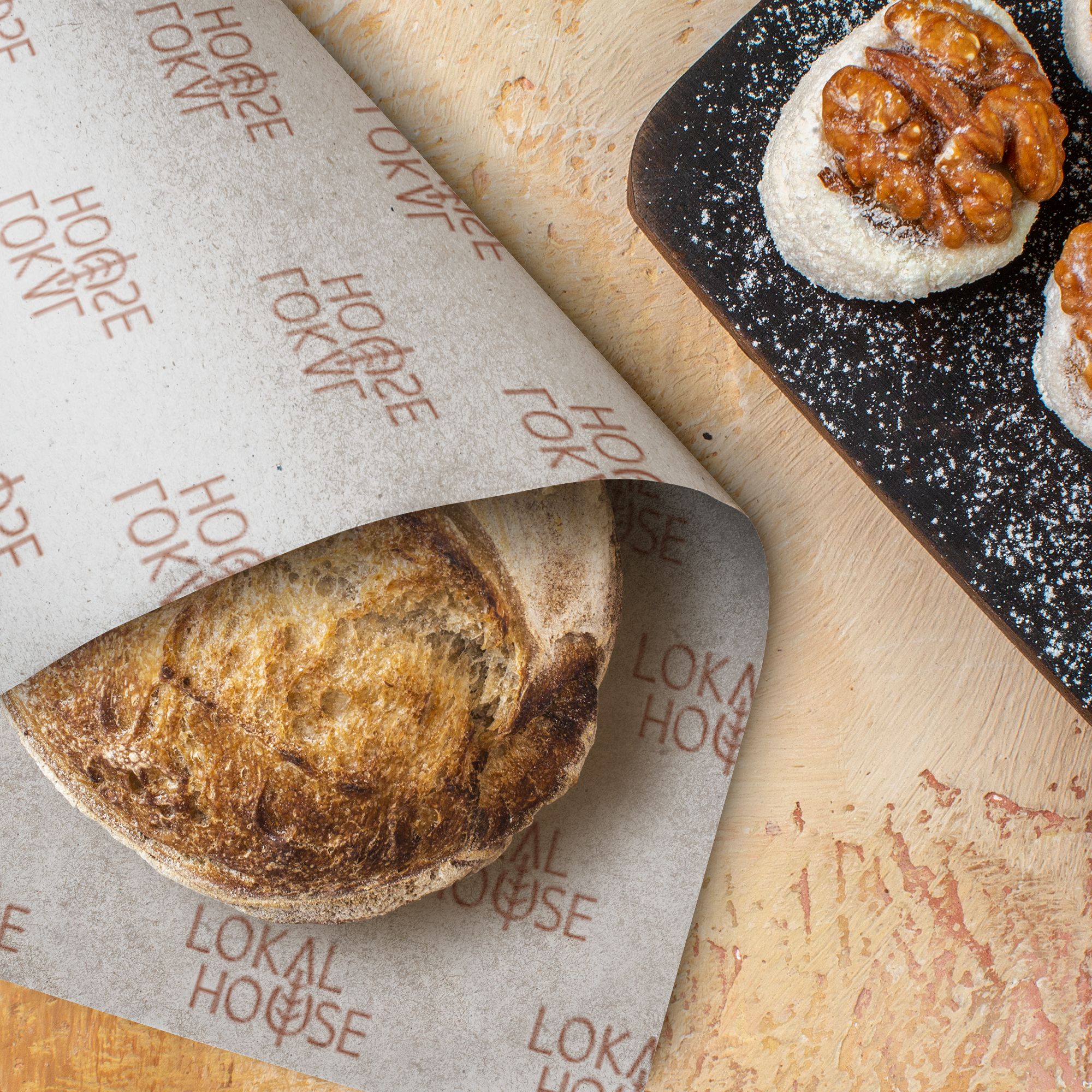 Artisanal sourdough bread wrapped in custom Lokal House parchment paper, paired with walnut pastries on a textured stone surface, highlighting the venue’s handcrafted food philosophy and branded tableware details.
