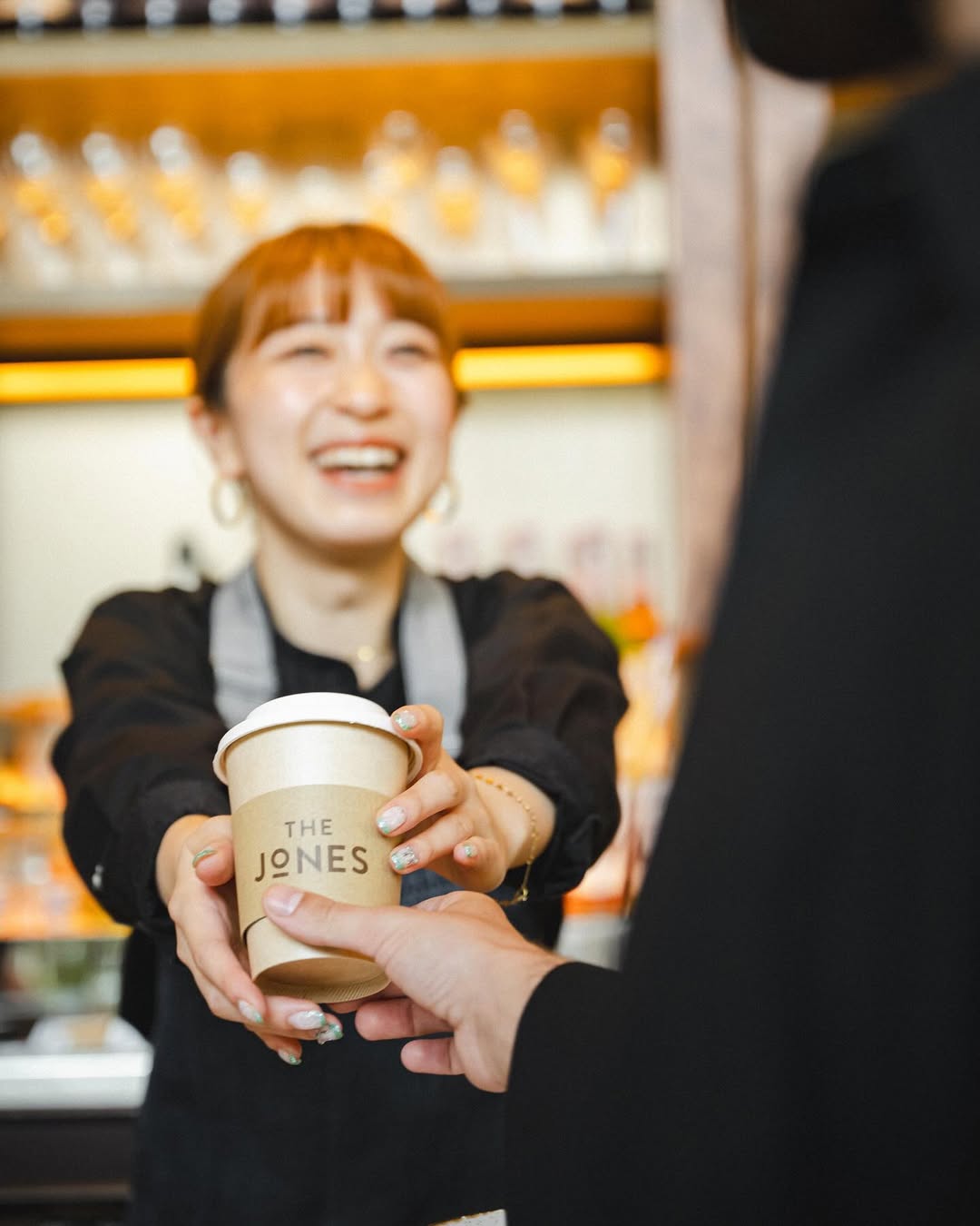 Barista handing a takeaway coffee cup branded ‘The Jones’ to a guest, capturing a warm service moment that reflects the café’s neighbourhood-focused concept and brand identity at Kimpton Shinjuku Tokyo.