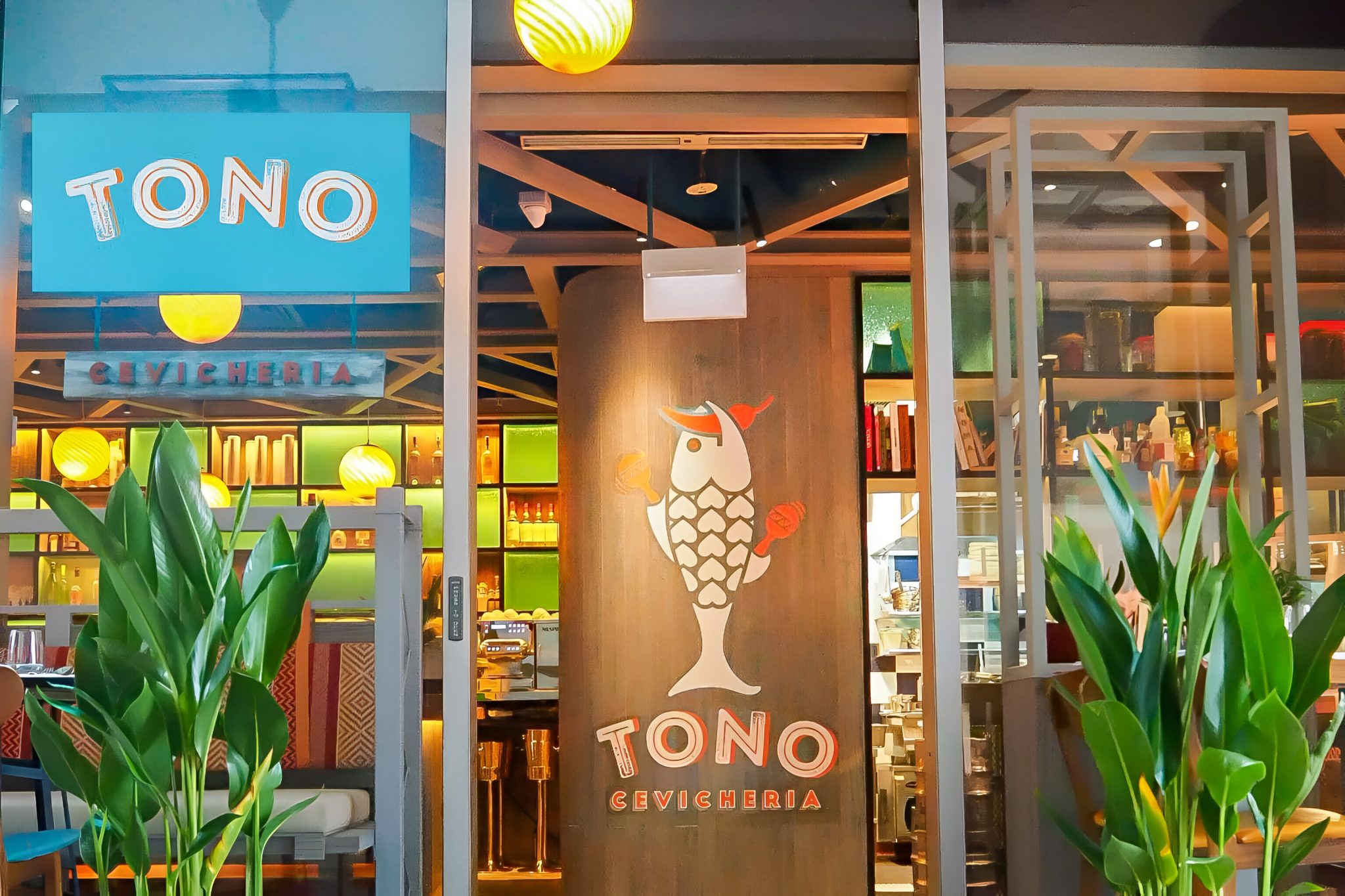 Entrance view of Tono Cevicheria in Singapore, featuring vibrant signage with a fish motif, tropical planting, and a colourful interior that reflects a lively, contemporary Latin dining concept designed by a hospitality branding agency.