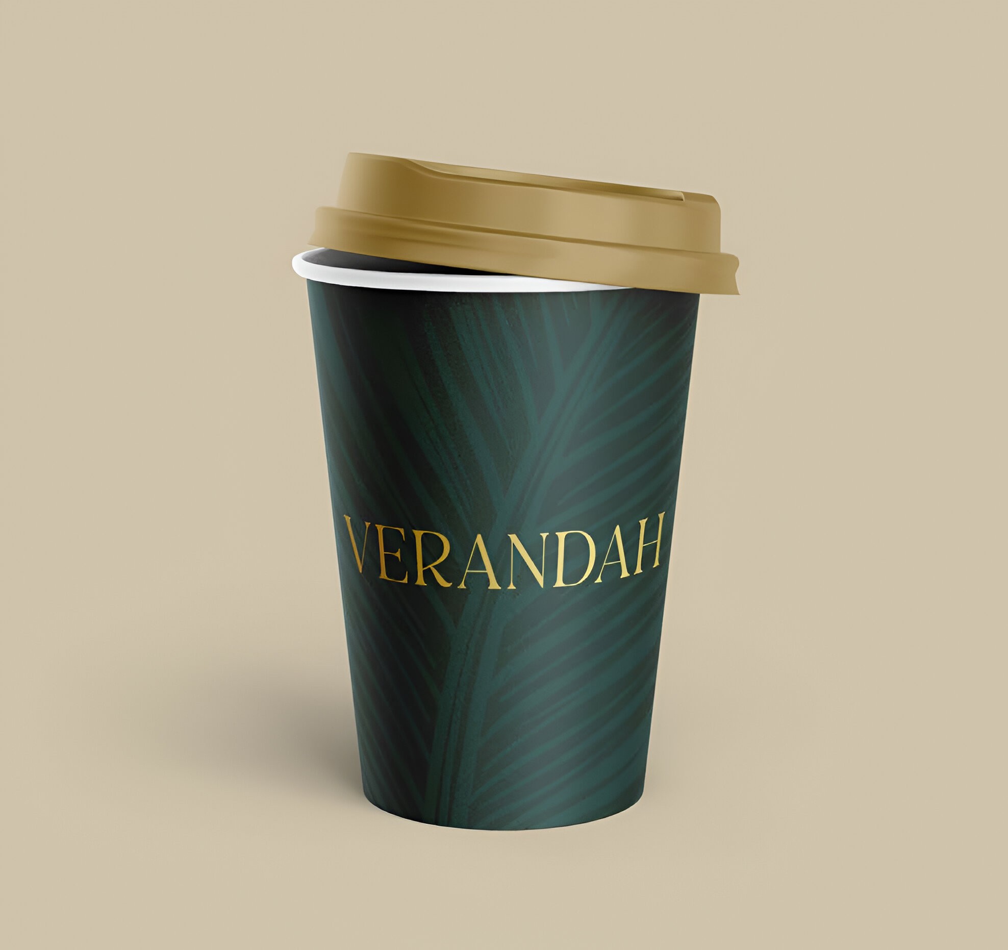 Verandah branded takeaway coffee cup with gold logo on a deep green, tropical leaf-patterned sleeve, finished with a beige lid against a neutral background.